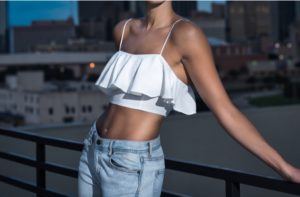 Attractive Slender Woman in a Crop Top and Jeans, against a Rail